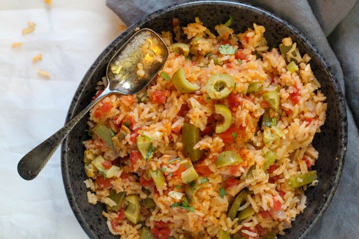 Mexican green rice served in a black bowl with green bell peppers and tomatoes and topped with green olives