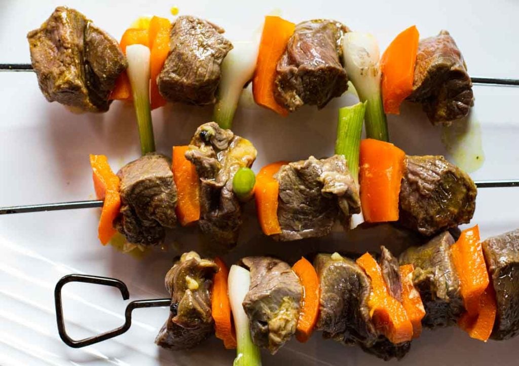Metal skewers with sirloin steak chunks, orange bell pepper and green onion