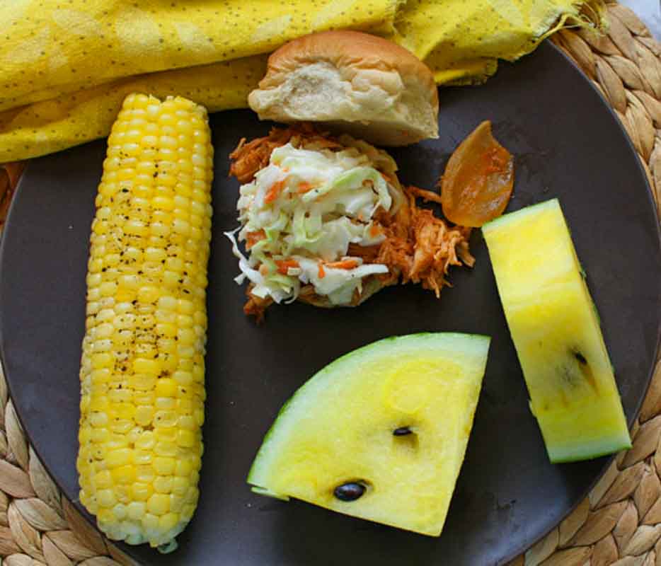 Crockpot bbq chicken sandwich with corn on the con and yellow watermelon slices.