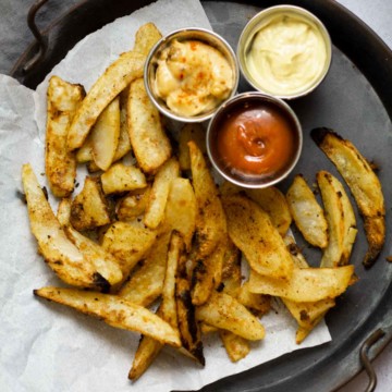 Oven fries on a metal tray with three dipping sauce.
