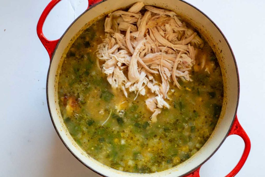 Adding shredded rotisserie chicken and broth to vegetables for rotisserie chicken soup