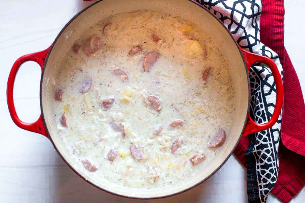 Creamy sauerkraut soup with potatoes and sausage in a Dutch oven.