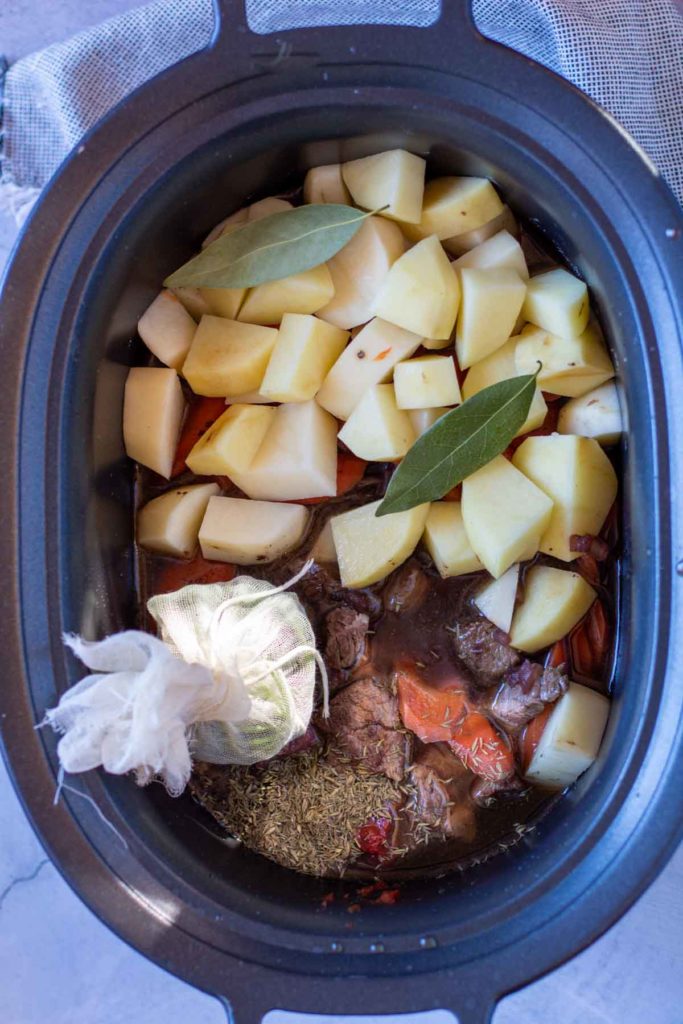 Adding ingredients to crockpot to make slow cooker beef stew.
