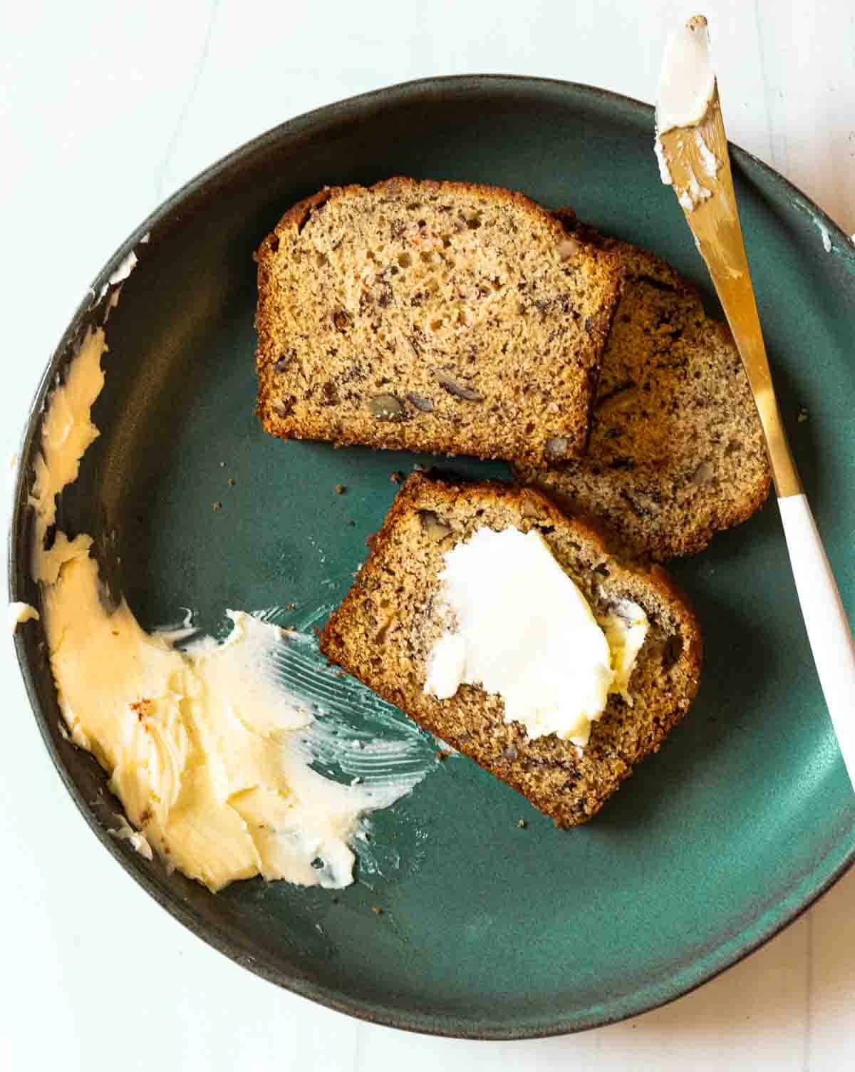 Sliced old fashioned Banana Nut Bread on a plate with butter.