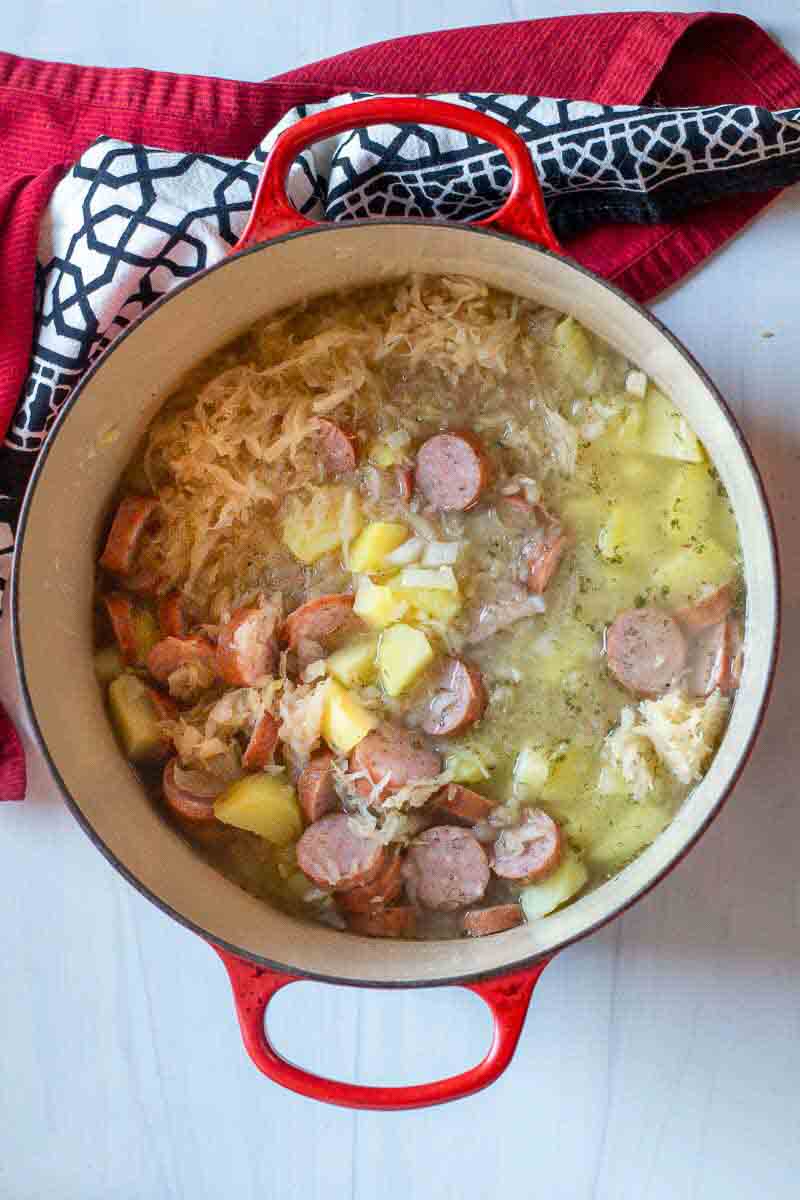 Sauerkraut soup with potatoes and sausage cooking in a Dutch oven.