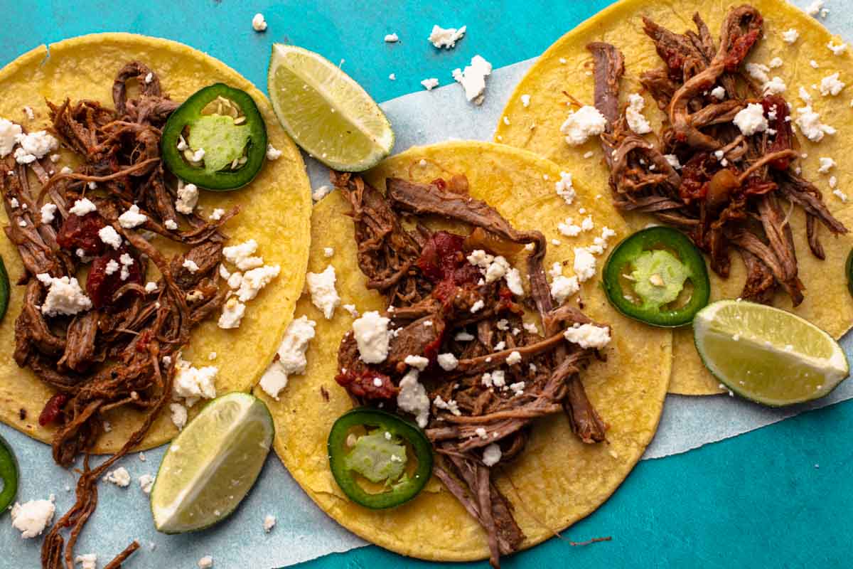 Tri-tip tacos on corn tortillas topped with cotija cheese, sliced jalapeno pepper and lime wedges.
