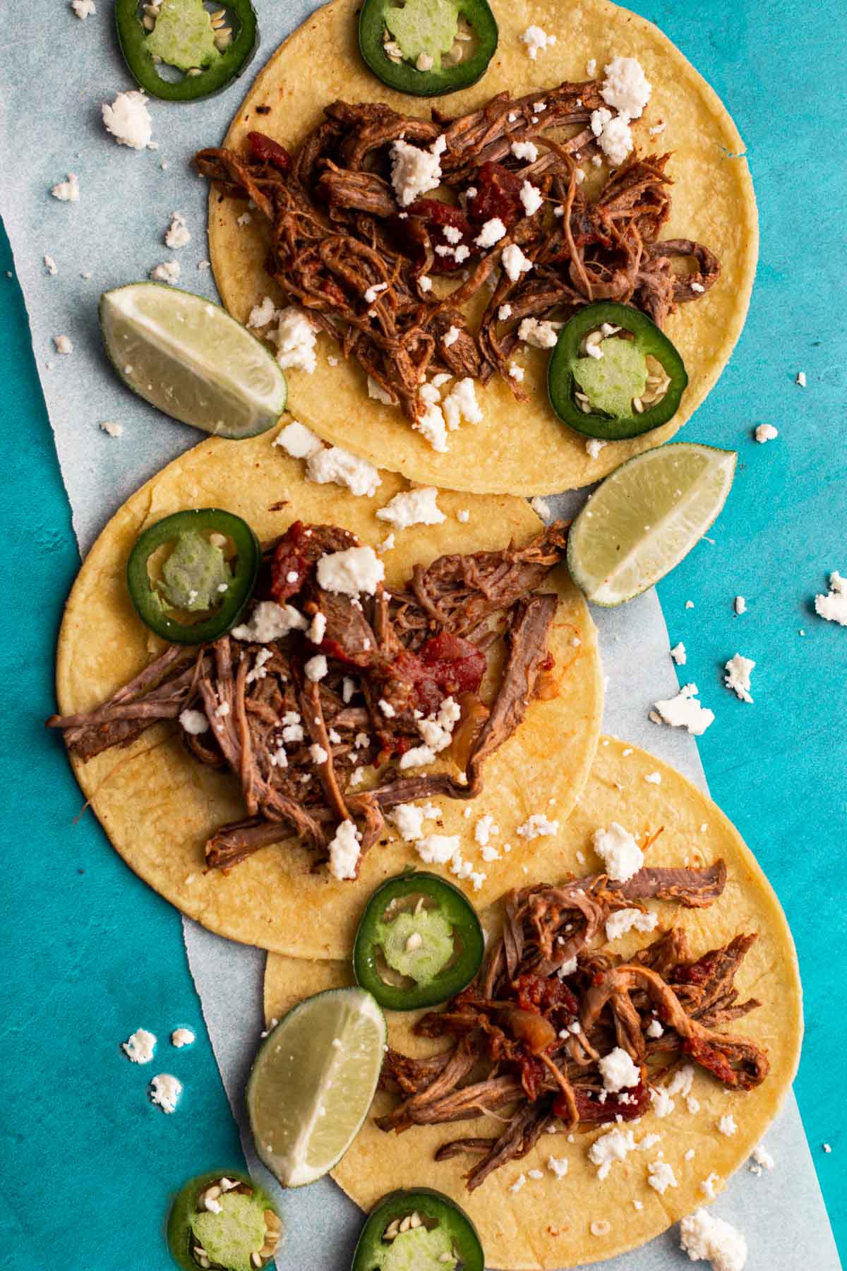 3 tri-tip tacos garnished with jalapeno peppers, lime wedges and cotija cheese.