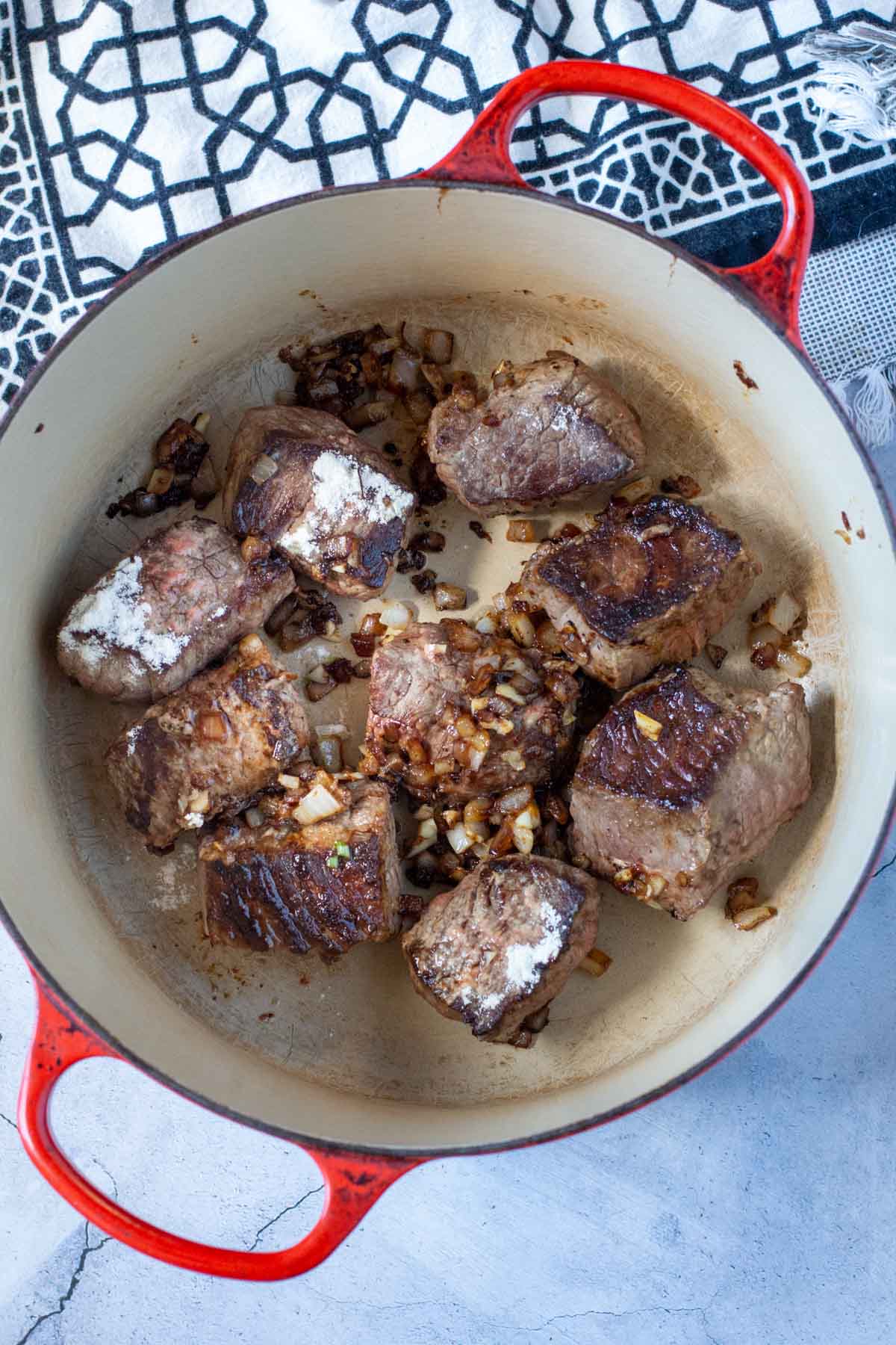 Chunks of chuck roast and onions in a dutch oven, to make red wine beef stew.