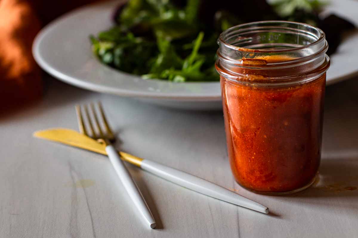 Homemade catalina dressing in a mason jar with a tossed salad in the background.