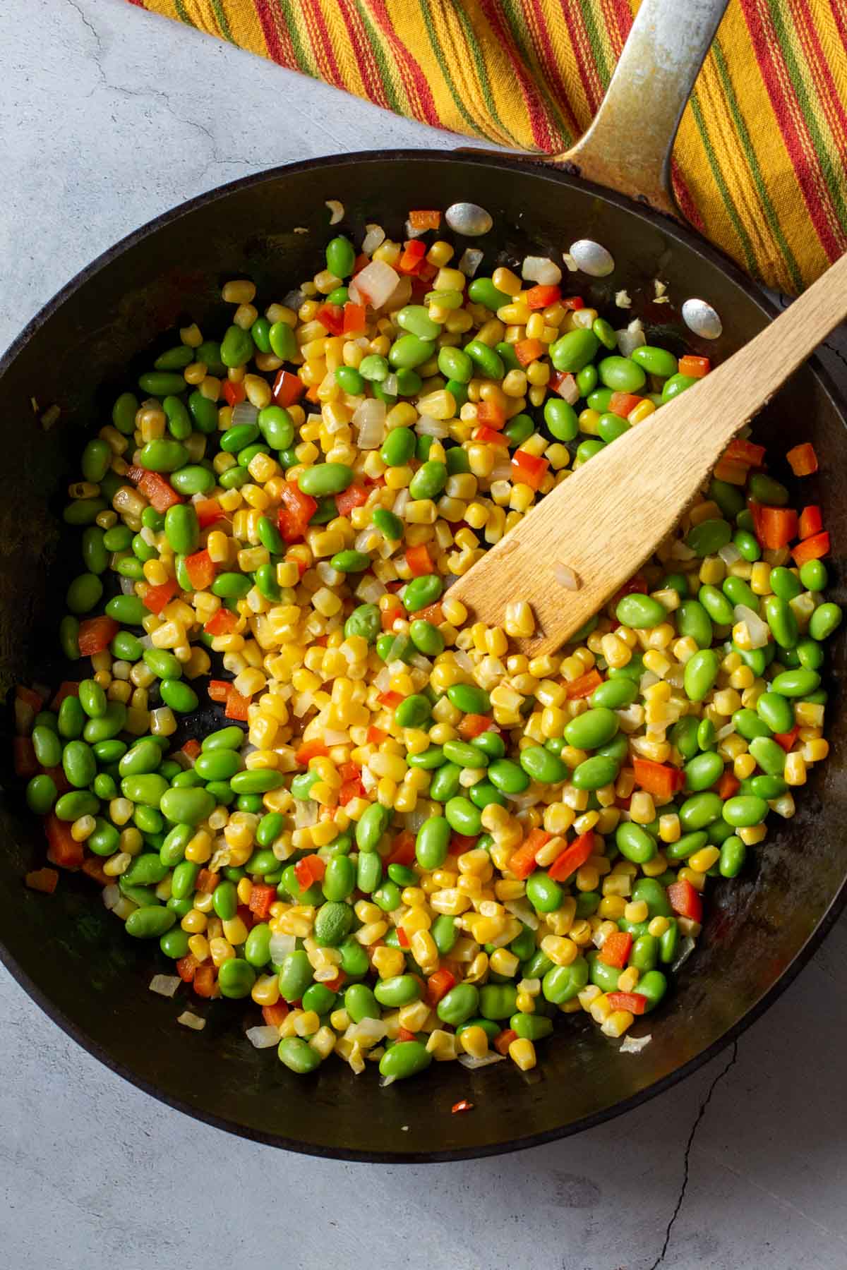 Cooking corn and edamame in a fry pan to make corn succotash.