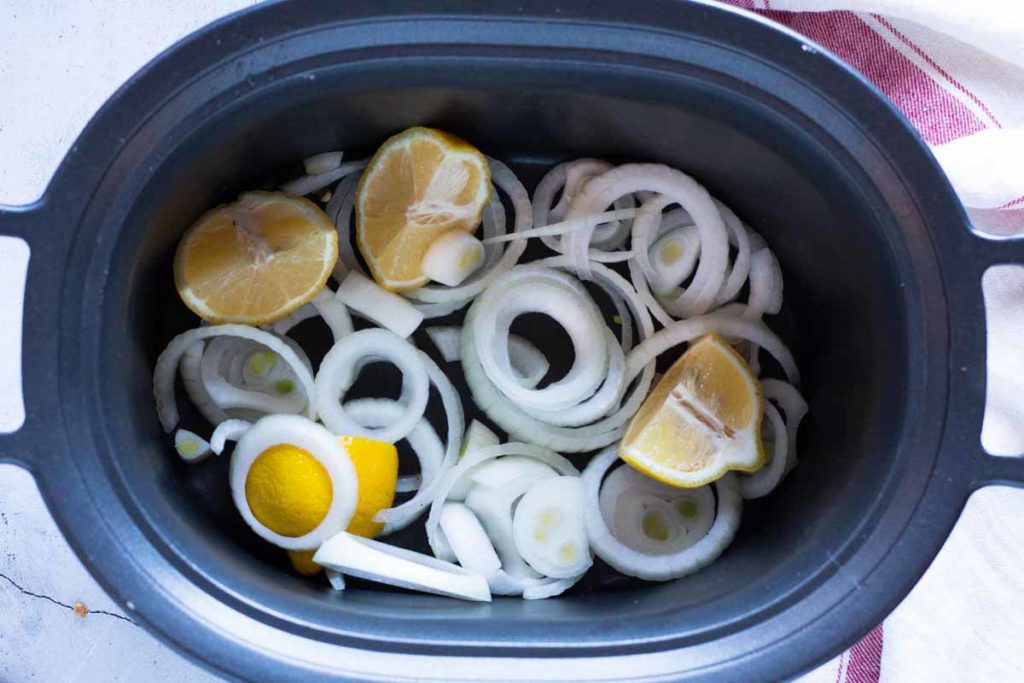 Placing onions and lemons in the bottom of the crockpot.