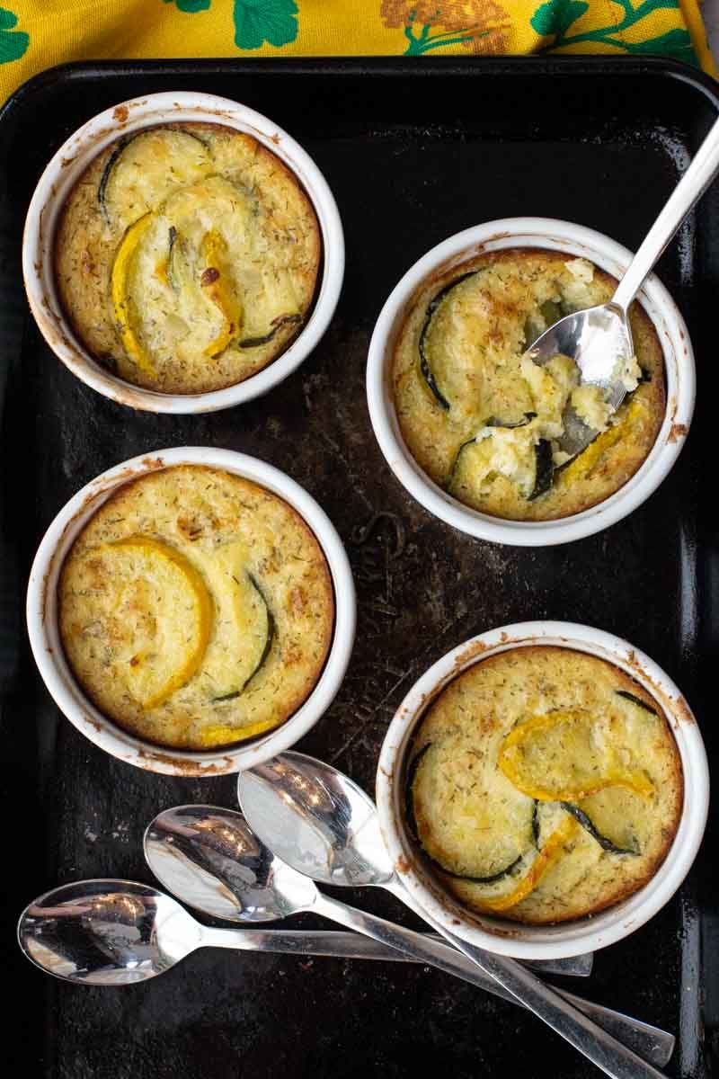 Individual baked zucchini casseroles in ramekins, baked and on a sheet pan.
