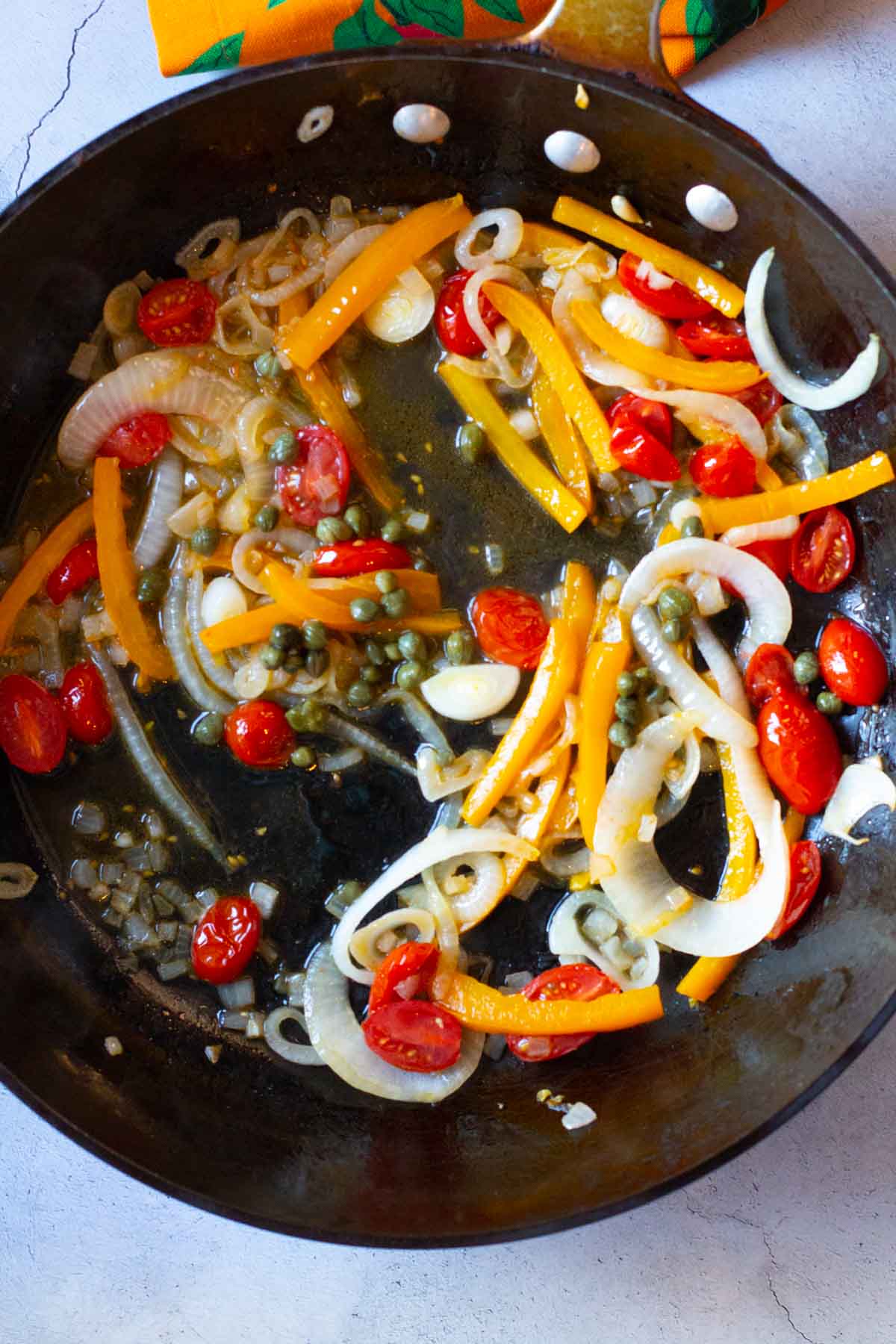 Adding capers to sauteed vegetables to make salmon pasta.