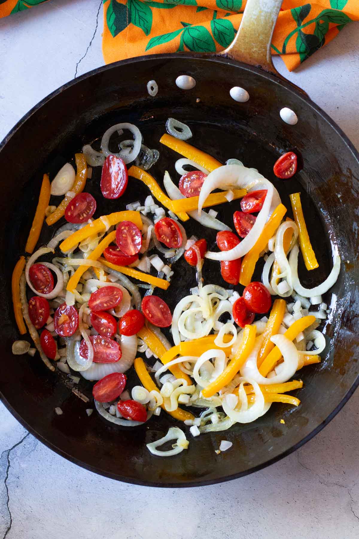 Adding tomatoes to vegetables to make salmon pasta.