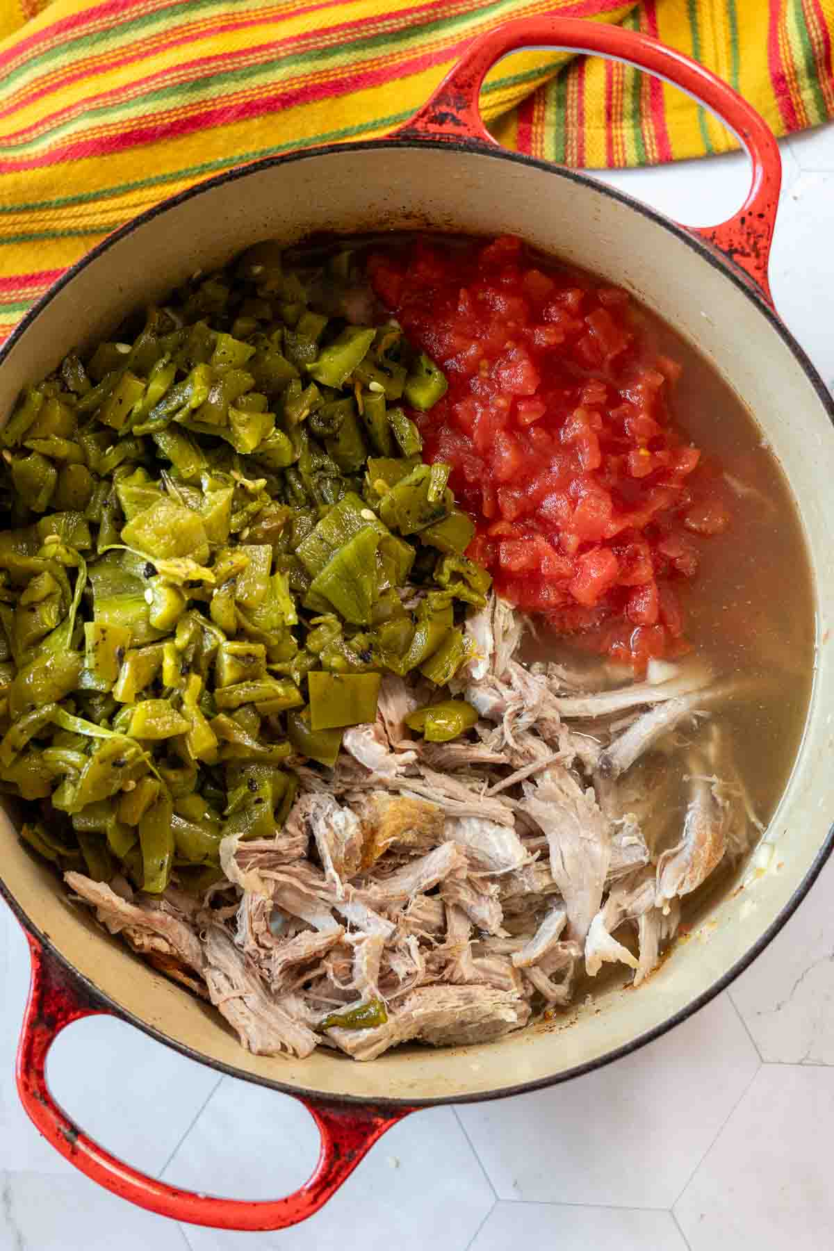 Adding shredded pork, tomatoes, and chopped chile peppers to pot to make Hatch Green Chili Colorado.