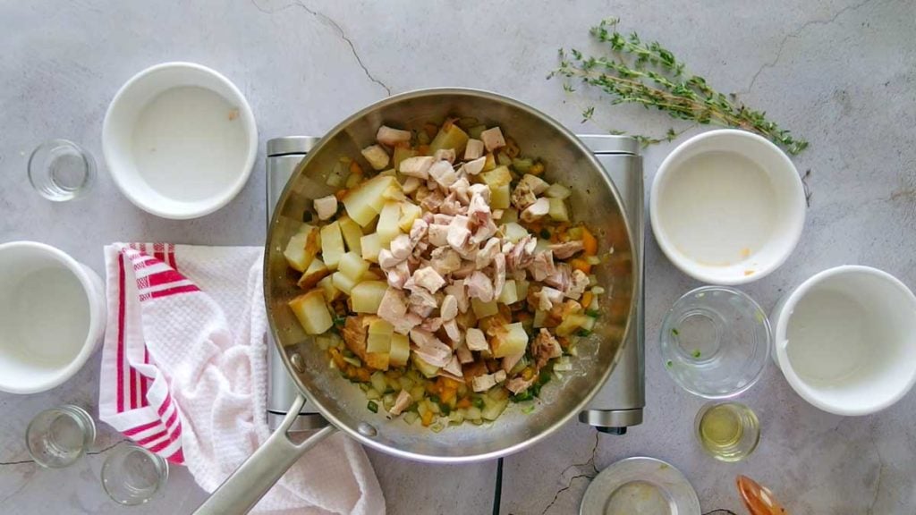 Adding chicken to vegetables and potatoes to make chicken hash