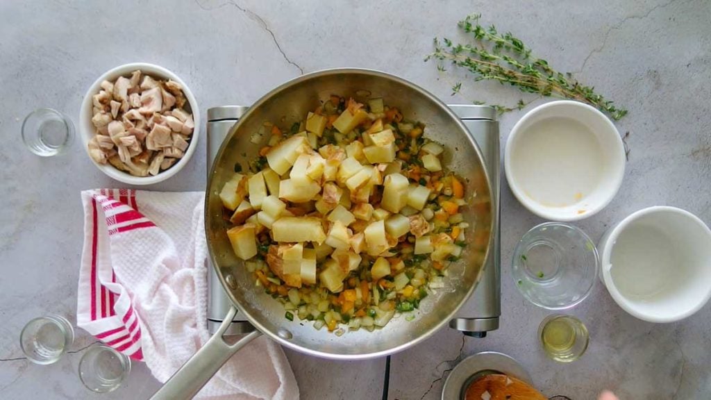 Adding potatoes to vegetables to make chicken hash