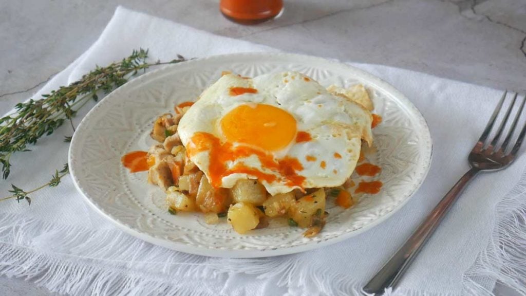 Chicken potato hash topped with a fried egg and drizzled with hot sauce.