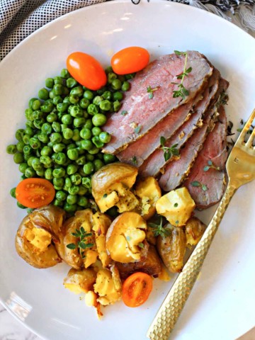 Baked tri-tip roast sliced and served with smashed potatoes and peas