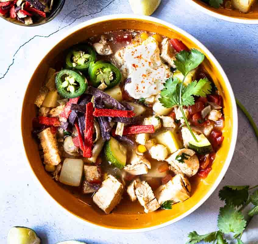 A bowl of southwest chicken soup with zucchini.