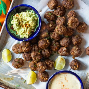 Mexican meatballs on a sheet pan with a bowl of guacamole and queso blanco.
