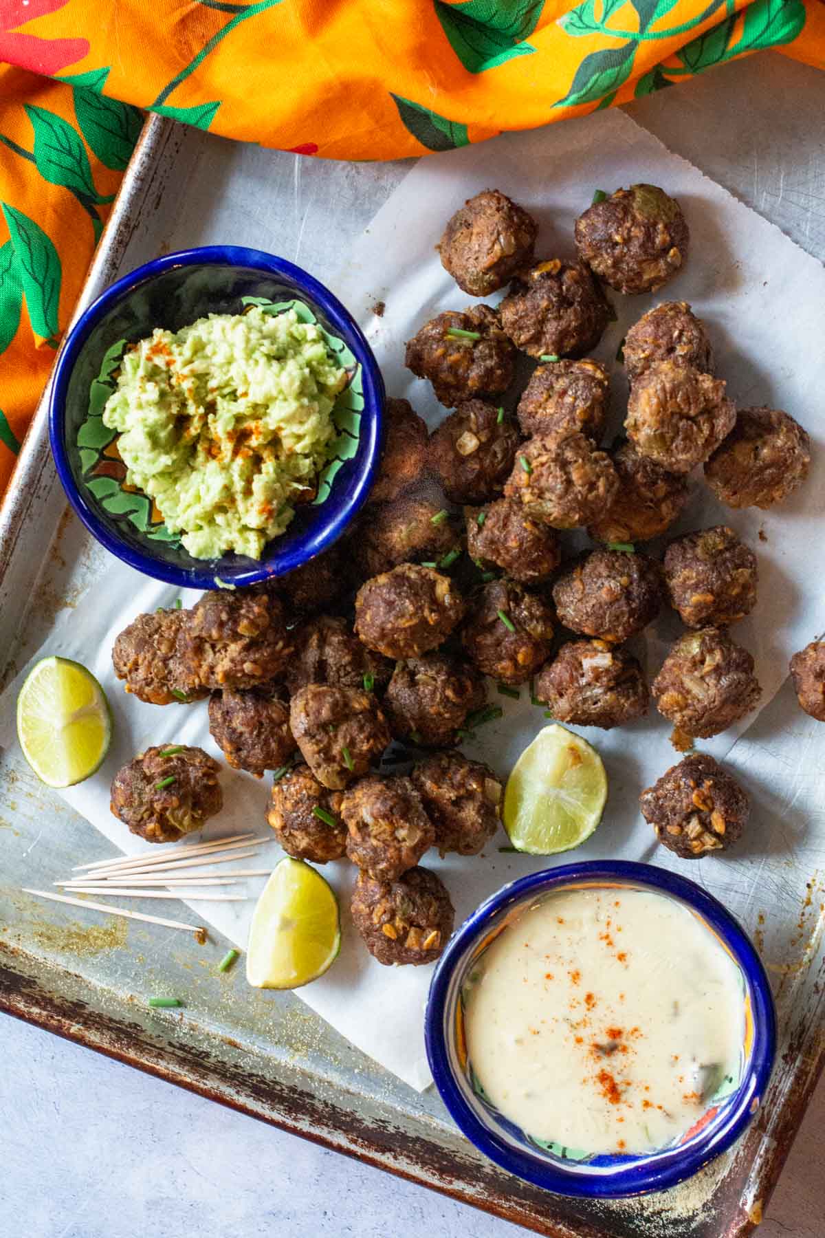Mexican meatballs on a sheet pan with a bowl of guacamole and queso blanco.