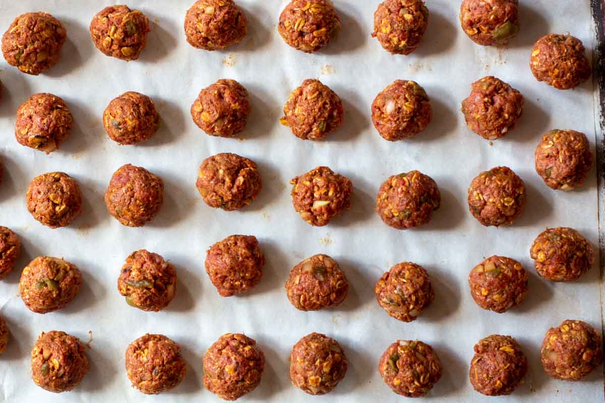 Uncooked mexican meatballs on a sheet pan with parchment paper.