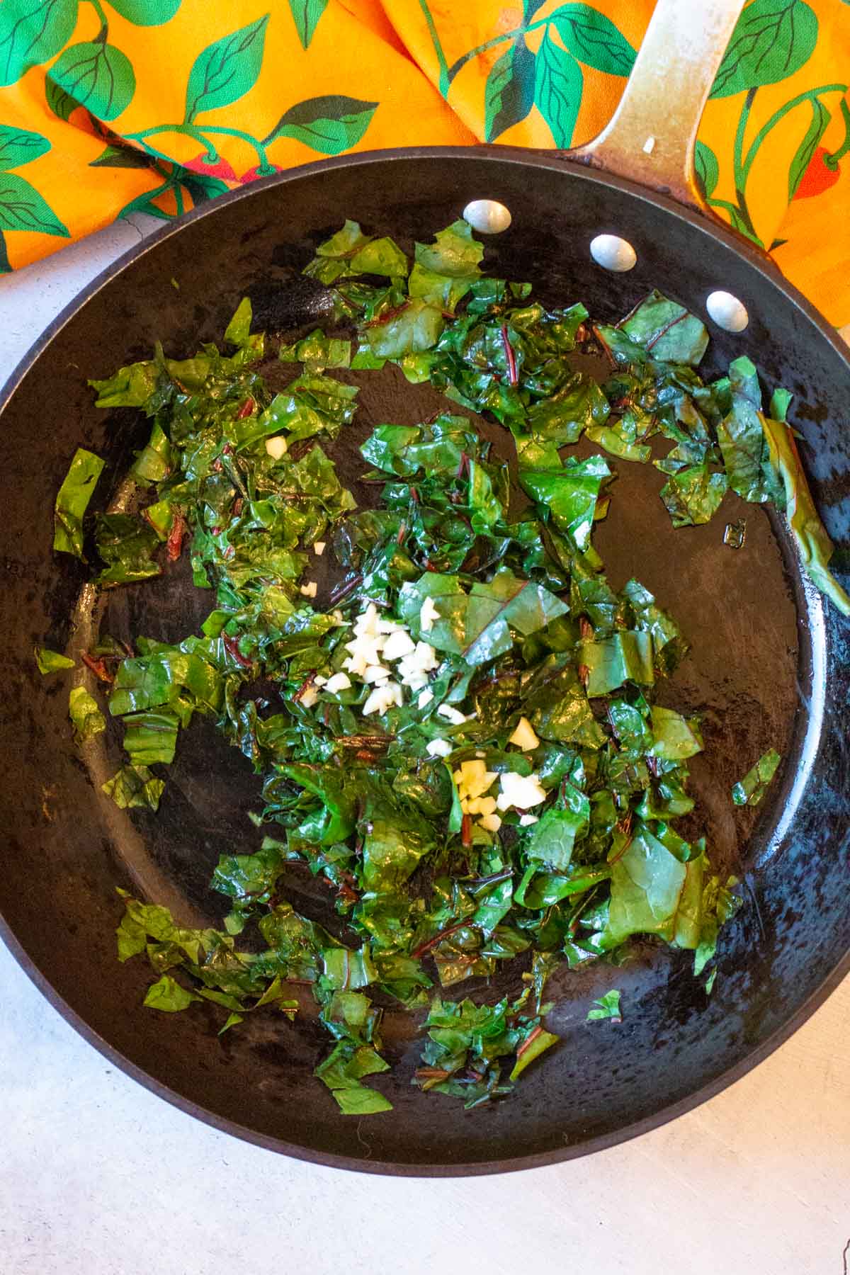 Cooking chopped Swiss chard in a fry pan with garlic.