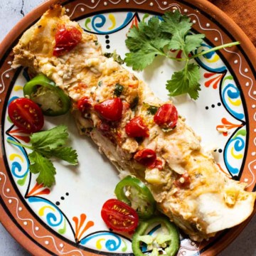 Shrimp burrito on a Mexican plate garnished with tomatoes and cilantro.