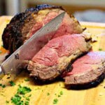 A cooked and sliced prime rib roast on a wood cutting board.