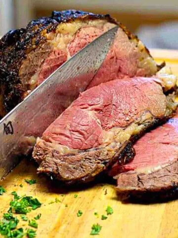 A cooked and sliced prime rib roast on a wood cutting board.