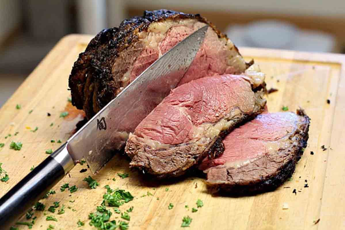 Slicing a Cooked bone-in prime rib roast on a cutting board.