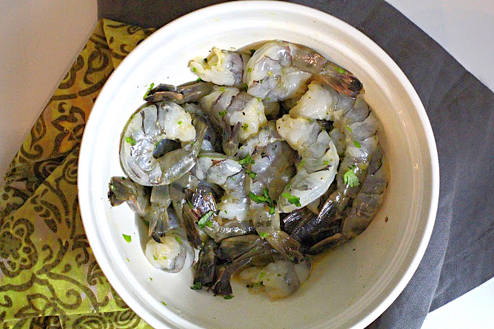 Raw shrimp in a white bowl with a marinade of orange juice and cilantro