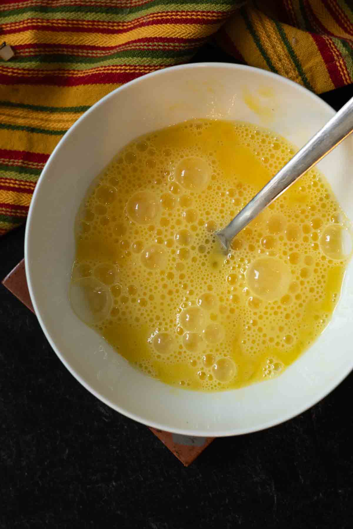 Beating raw eggs to make scrambled eggs for breakfast burritos with potatoes.