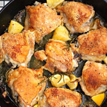 Cast Iron Skillet rosemary braised chicken thighs with lemon wedges cooking on a wire rack.