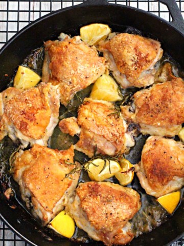 Cast Iron Skillet rosemary braised chicken thighs with lemon wedges cooking on a wire rack.