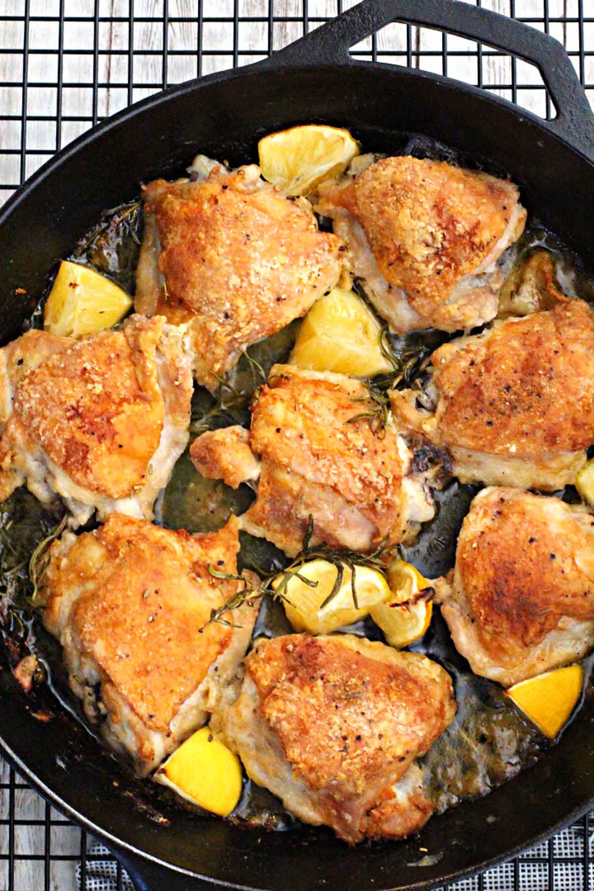 Cast Iron Skillet rosemary braised chicken thighs with lemon wedges cooking on a wire rack.