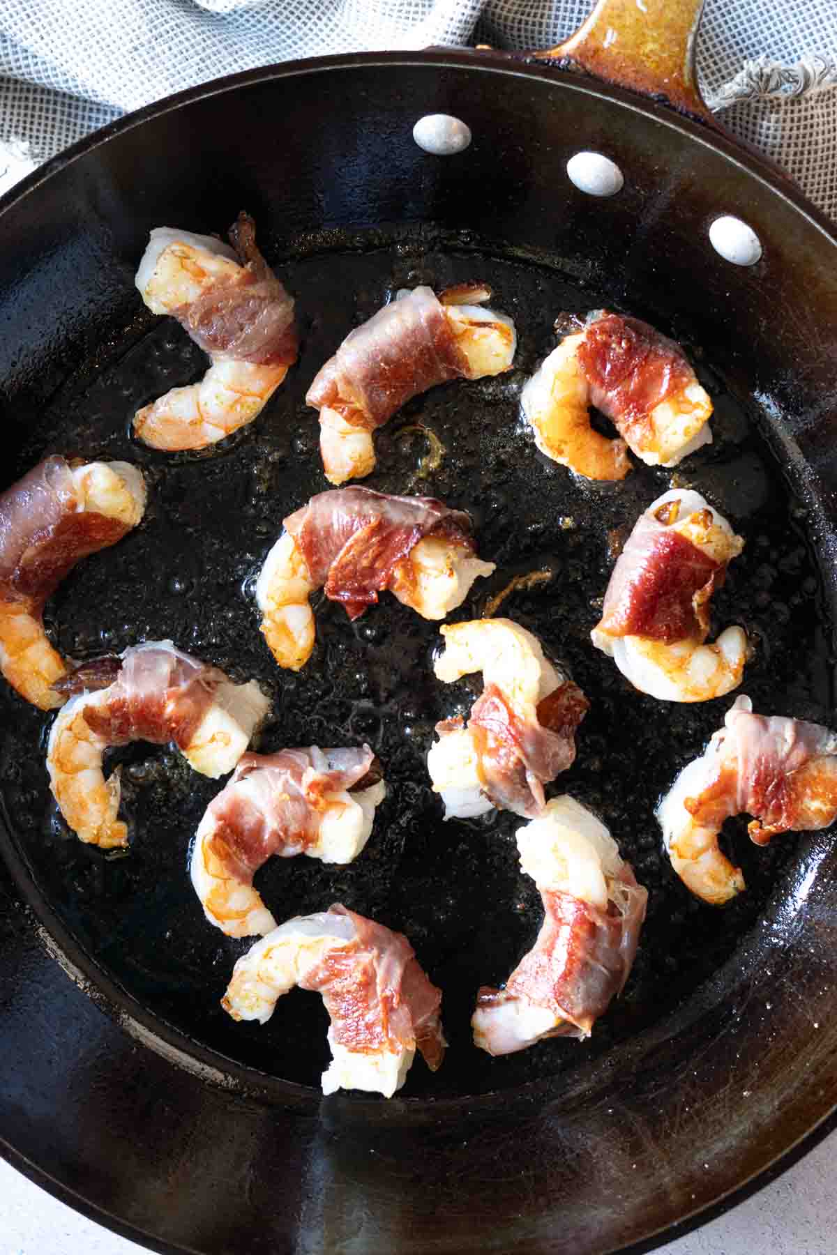 Frying prosciutto wrapped shrimp in a large frr pan.