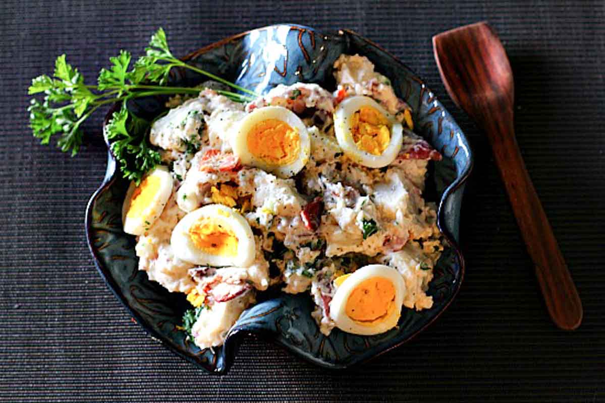 Bacon Blue Cheese Potato Salad in a blue ceramic bowl topped with sliced hard boiled eggs