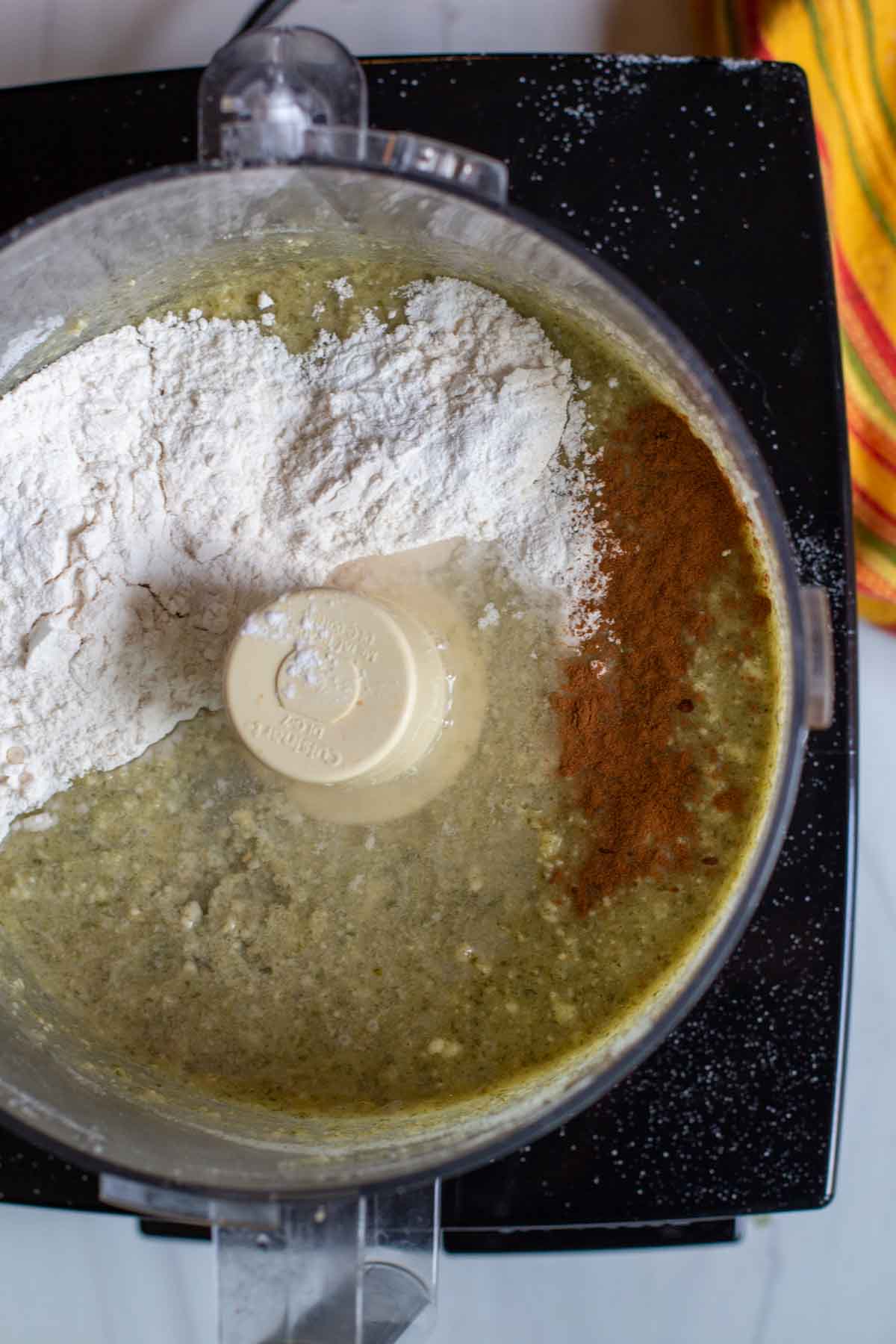 Adding flour and cinnamon to make a Mexican chocolate cake in a food processor.