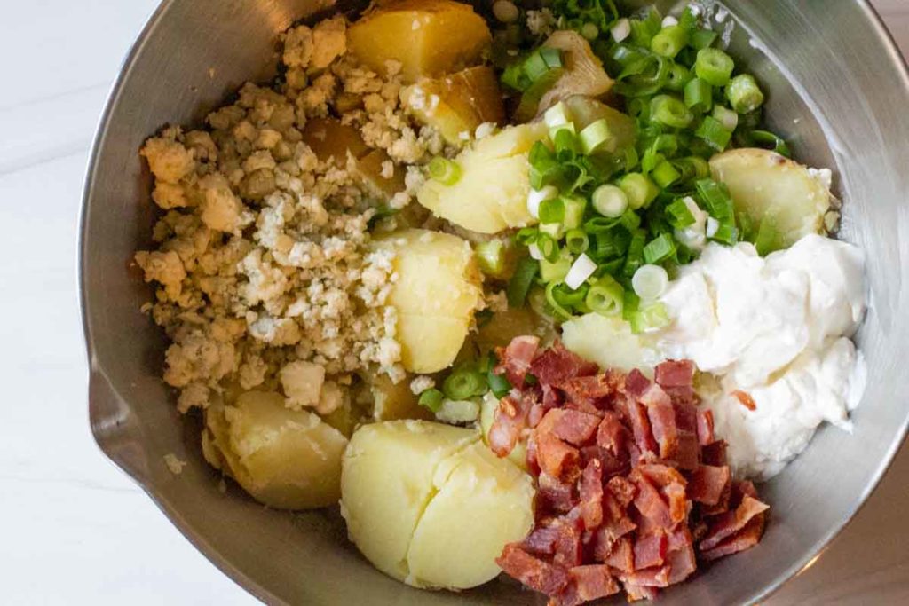 Cooked potatoes, onions, bacon and blue cheese in a large silver bowl.