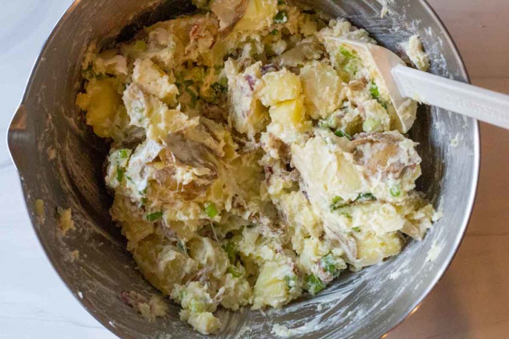 mixing ingredients together in a mixing bowl for potato salad with bacon