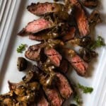 Sliced bavette steak on a white platter topped with cognac mushroom cream sauce.