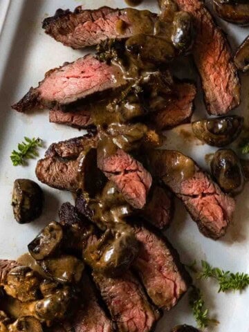 Sliced bavette steak on a white platter topped with cognac mushroom cream sauce.