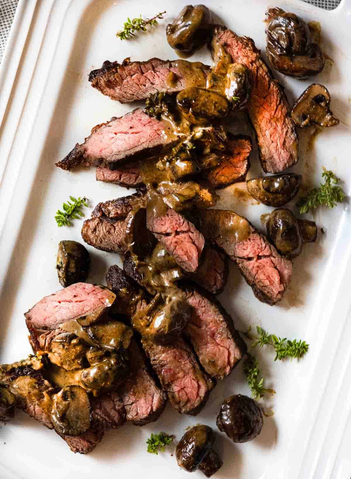 Sliced bavette steak with cognac creamed mushrooms on a white platter.