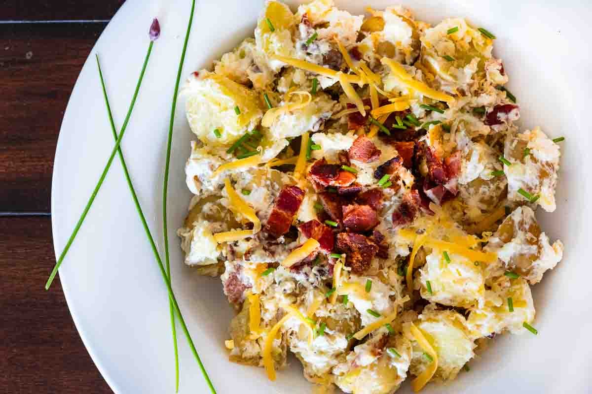 Potato salad with bacon served in a white bowl garnished with chives.