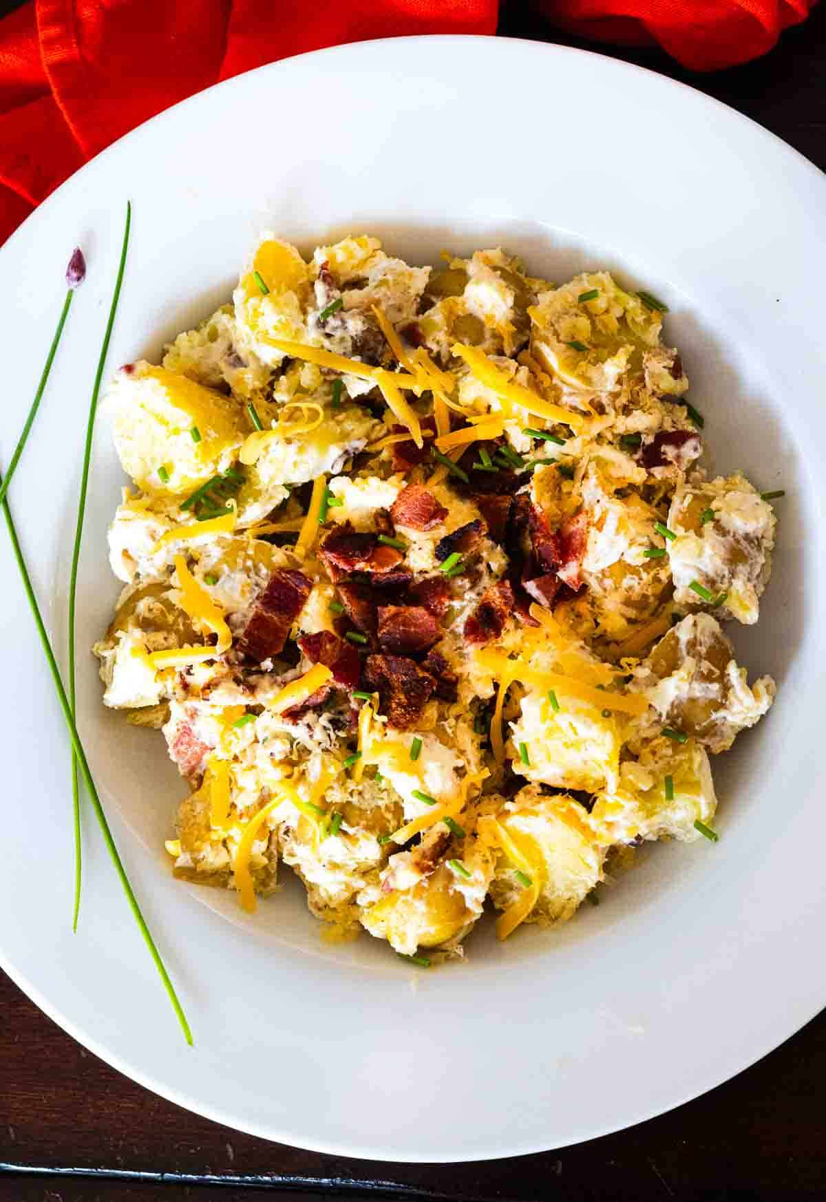 Loaded Baked Potato Salad with Bacon served in a white bowl and garnished with chives.