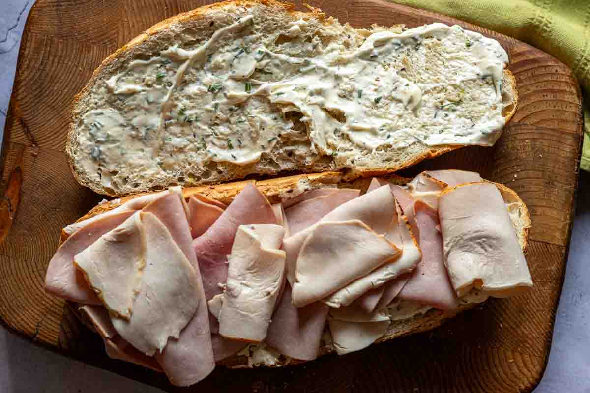 Building a sub club sandwich by placing deli meat on bread.
