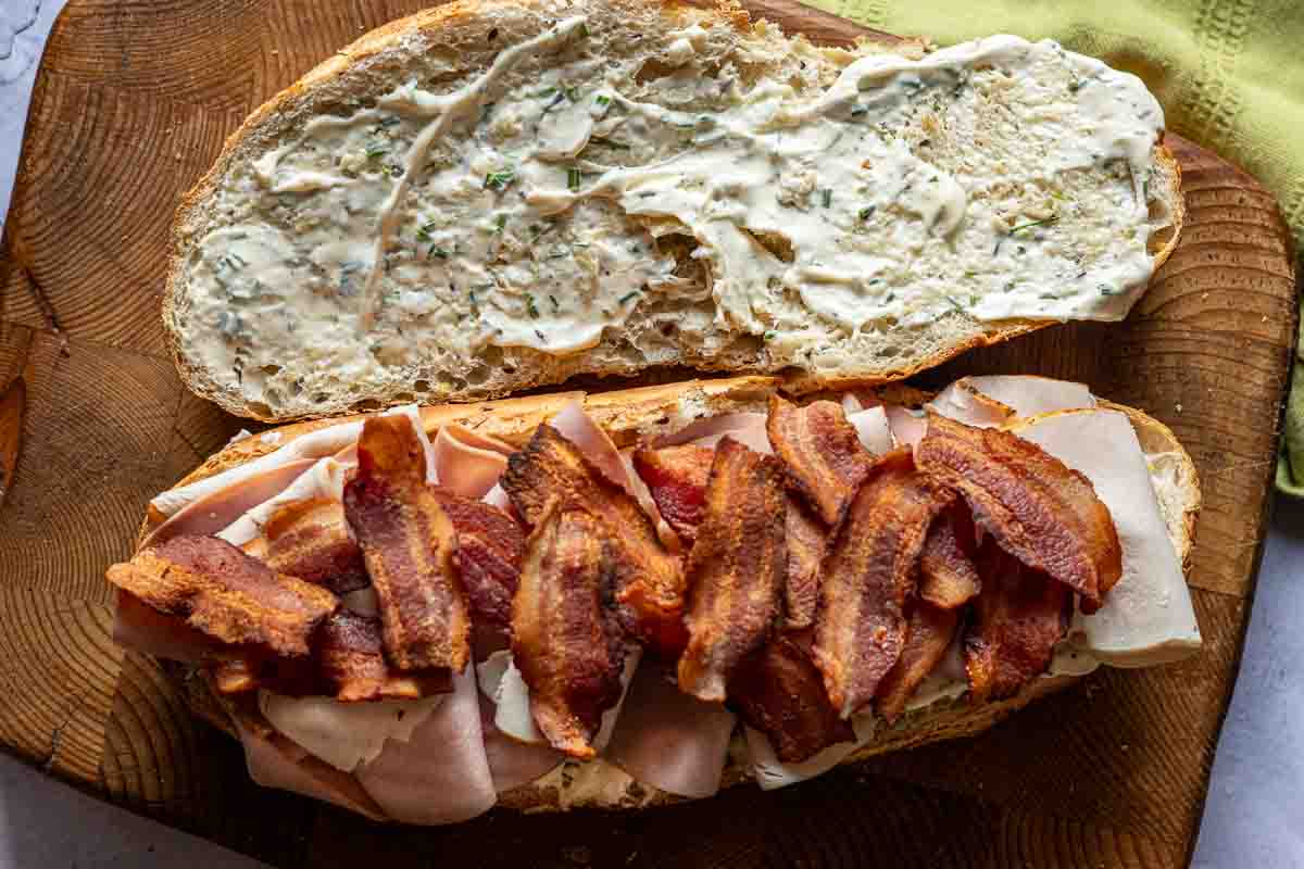 Adding bacon to a homemade club sandwich.