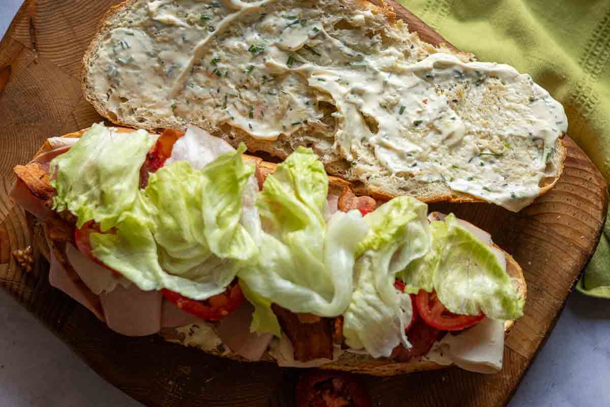 Adding lettuce to a sub club sandwich.